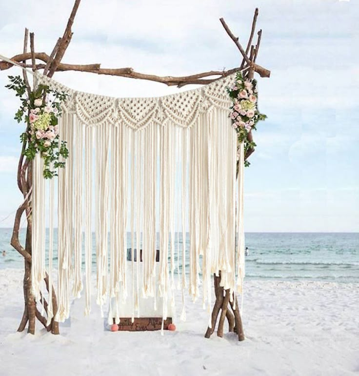 a wedding ceremony setup on the beach with white curtains and pink flowers hanging from branches