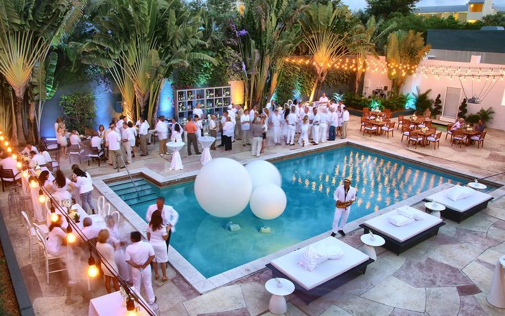 an aerial view of a pool with white balloons and people standing around it at night