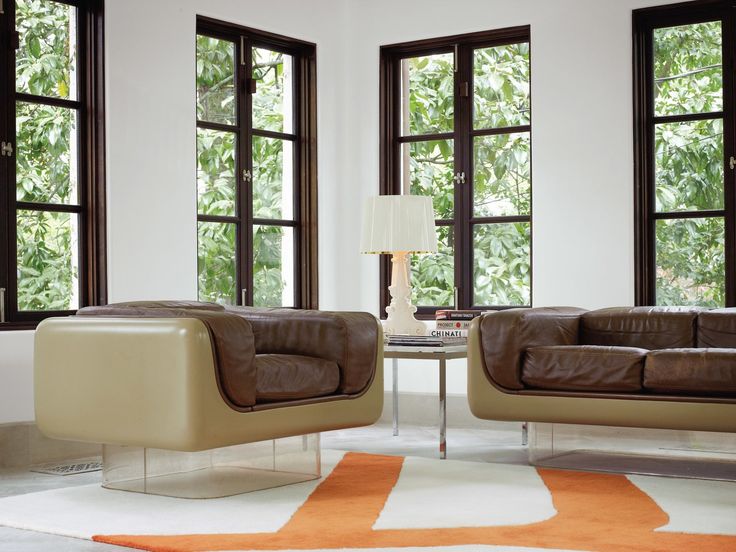 two brown leather couches in front of three windows with orange rug on the floor