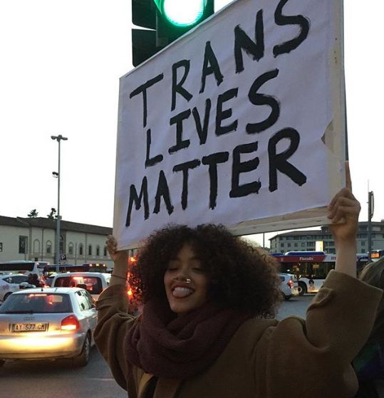 a woman holding up a sign that reads transs lives matter