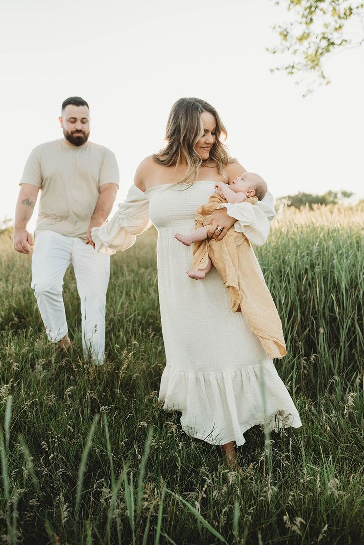 a man and woman walking through tall grass holding their baby