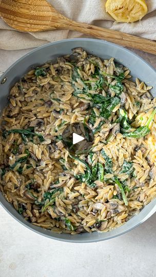 a pan filled with pasta and spinach on top of a white cloth next to wooden utensils