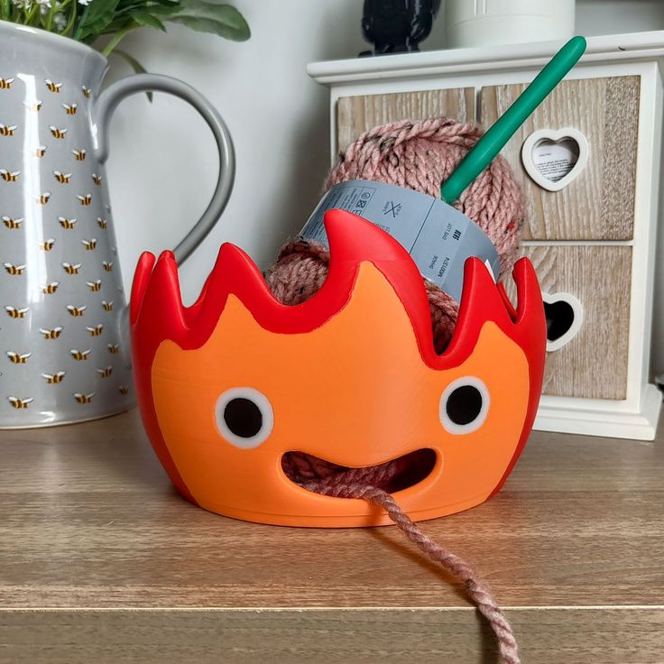 an orange and red fire mask on top of a wooden table next to a mug