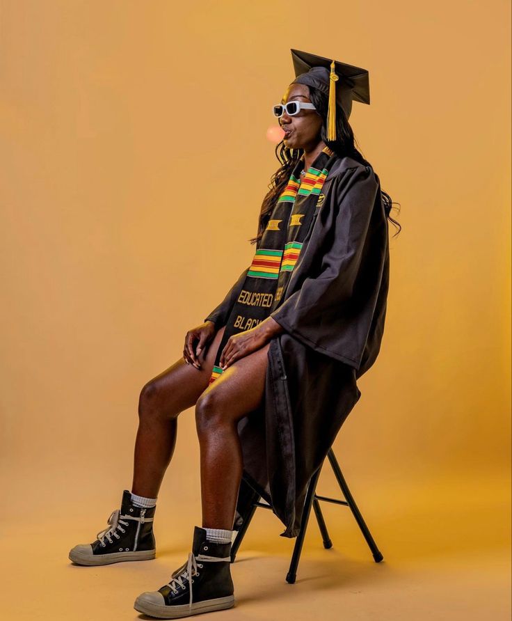 a man sitting on top of a chair wearing a graduation cap and gown in front of a yellow background