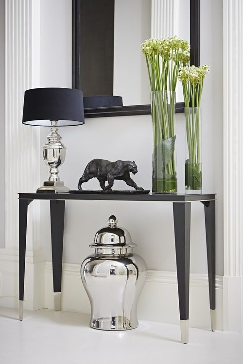 a black and white console table with vases on it, lamp and mirror in the background