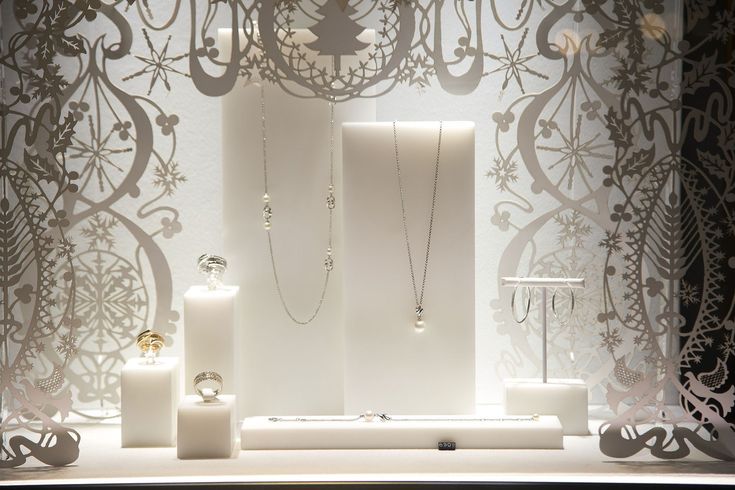 an assortment of jewelry displayed in front of a wall with intricate paper cutouts on it