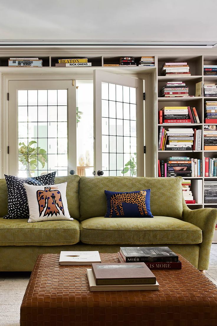 a green couch sitting in front of a window next to a coffee table and bookshelf