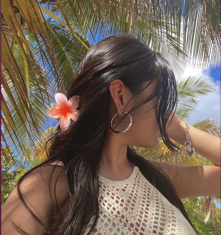 a woman with long hair wearing large hoop earrings and a flower in her left ear