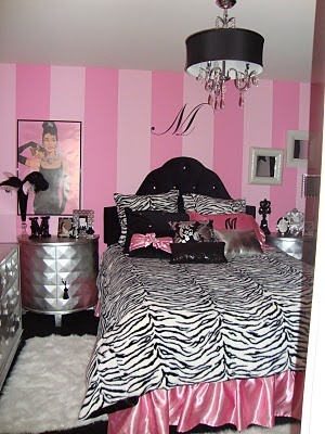 a bedroom decorated in pink and black with zebra print on the bed, dressers, and chandelier