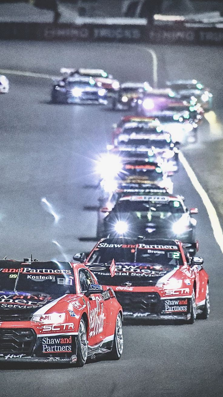 a group of cars driving down a race track with lights on the side of them