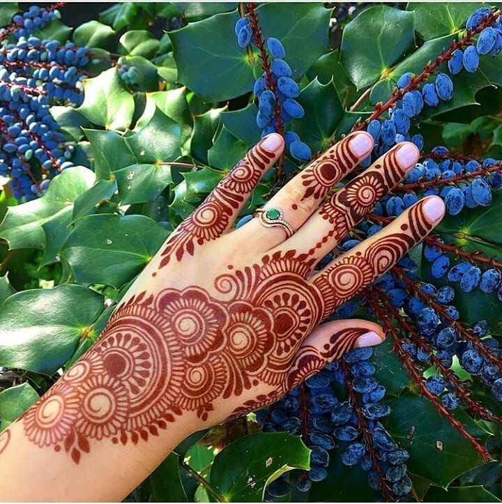 a woman's hand with henna on it and blue berries in the background