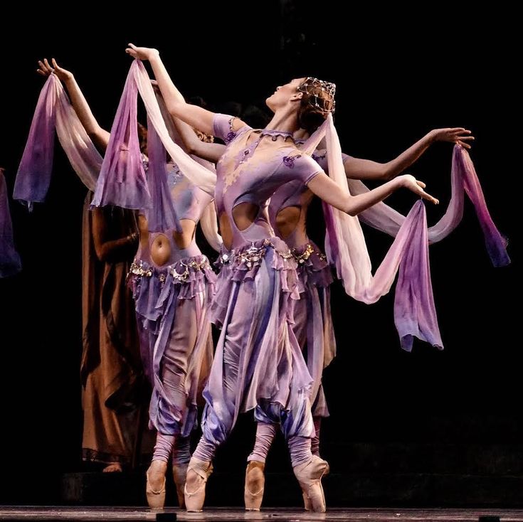 three women in purple outfits are performing on stage with their arms around each other while one woman is holding her leg up