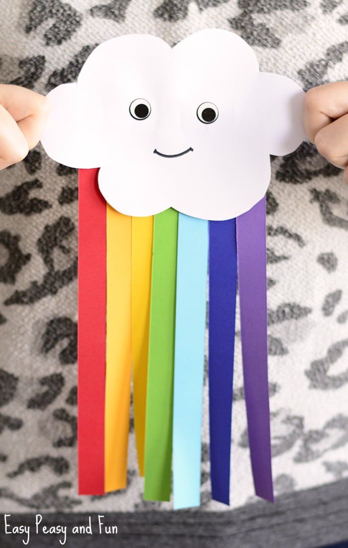 a person holding up a paper cloud with rainbows on the sides and black eyes