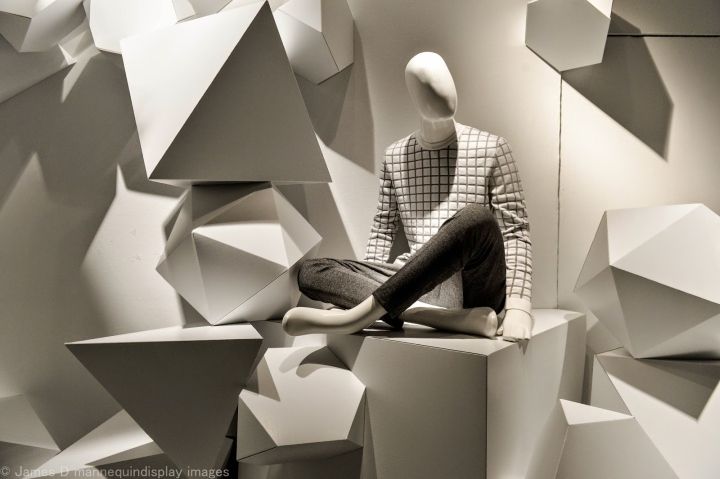 a mannequin sitting on top of a white cube in front of a wall