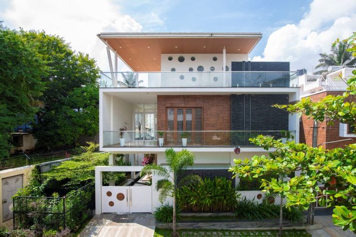 the house is surrounded by greenery and trees, with an open balcony above it