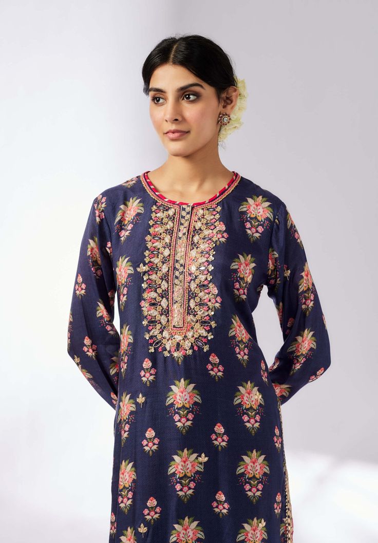 This smart, contemporary collection features a bold floral print, beautifully enhanced with delicate embroidery around the neck. The long-sleeved tunic, crafted from luxurious cotton silk, adds shimmer and richness to the ensemble. Easy to wear and versatile for any occasion, this tunic combines elegance with modern style. Note: Pants are for styling purposes only. Elegant Straight Kurta Tunic With Floral Embroidery, Blue Kurta With Embroidered Neckline For Festive Occasions, Elegant Floral Print Tunic Kurta, Festive Blue Kurta With Embroidered Neckline, Floral Print Top For Eid, Festive Long Sleeve Indigo Kurta, Elegant Blue Floral Print Kurta, Long Sleeve Indigo Kurta For Festive Occasions, Festive Floral Print Tunic