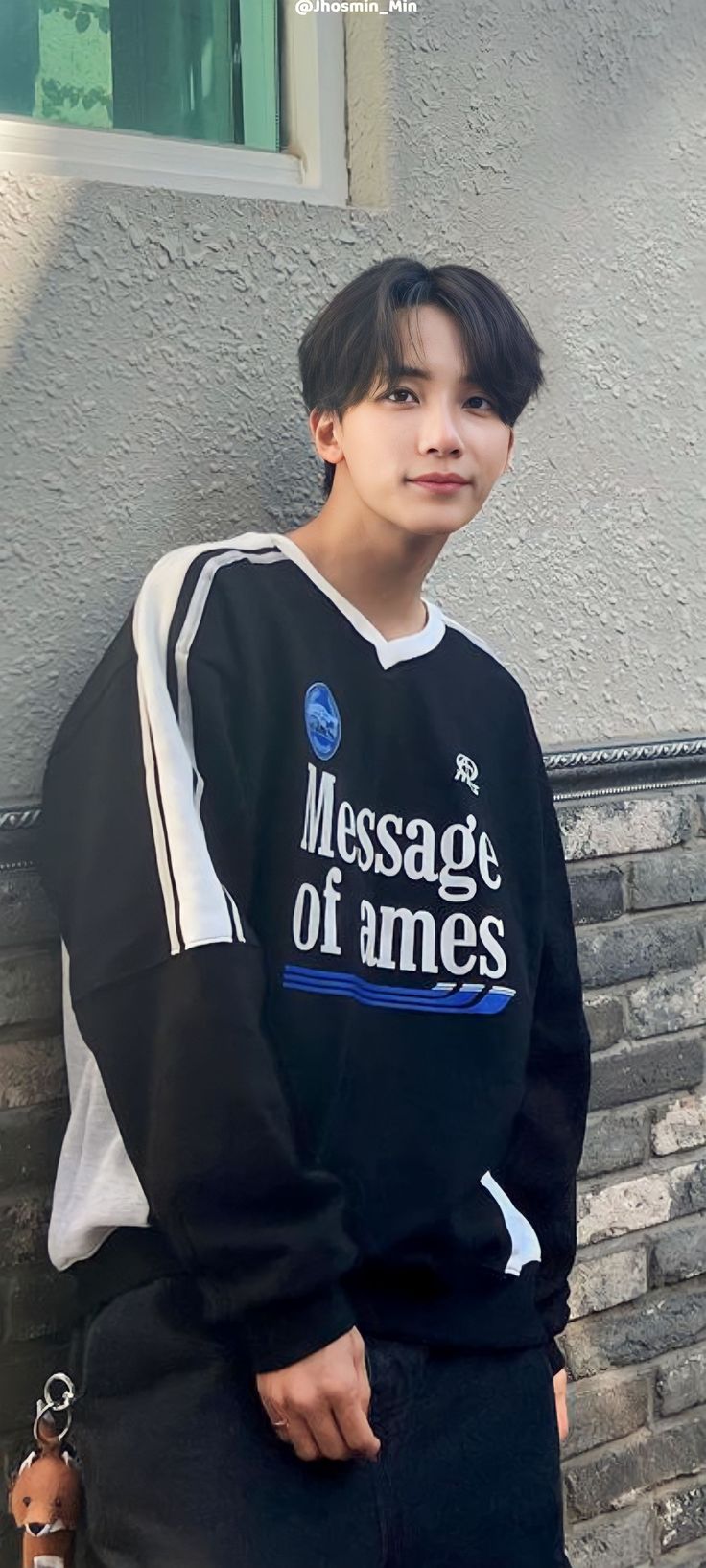 a young man standing next to a brick wall wearing a black sweatshirt with message of names on it