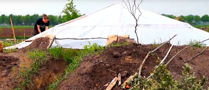 there is a man that is digging in the dirt near a tent and some trees