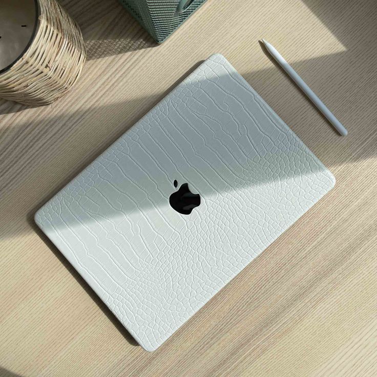 an apple laptop computer sitting on top of a wooden table next to a cup and pen