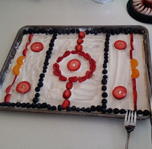 a cake with white frosting, red and black decorations is on a table next to a fork