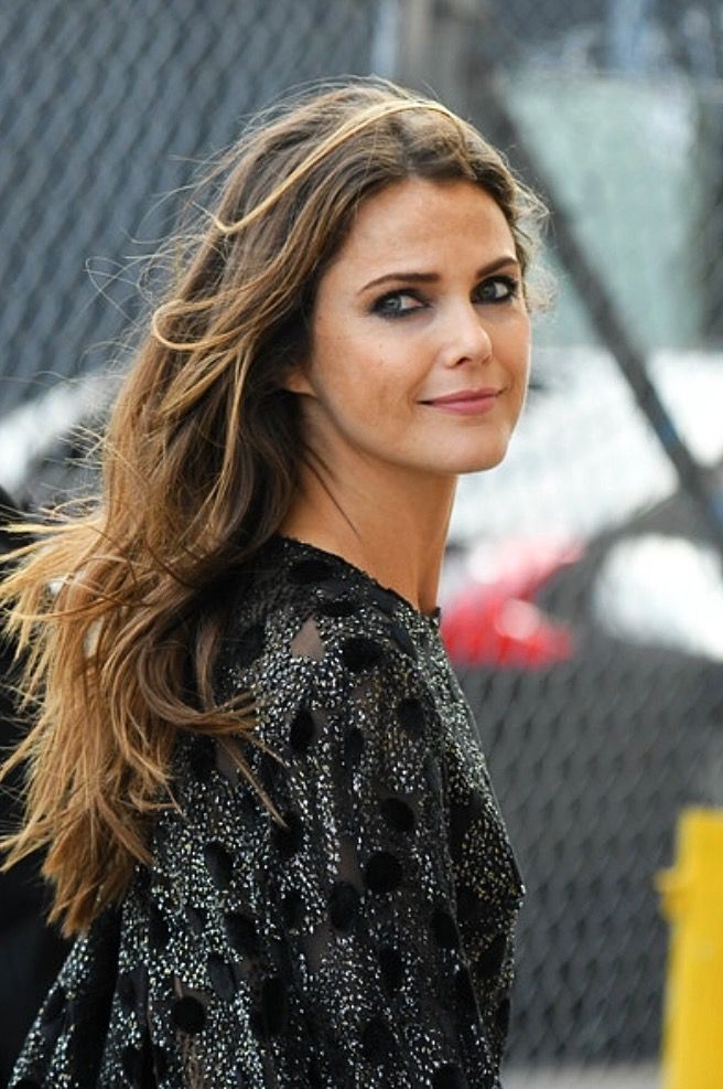 a woman with long hair is standing in front of a fence and looking at the camera