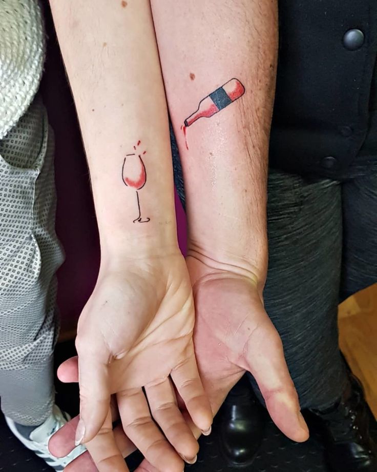 two people holding hands with tattoos on their arms, one has a wine glass and the other has a bottle