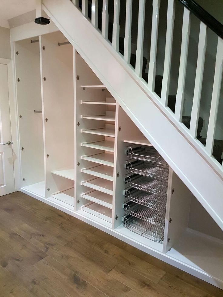 an open closet under the stairs in a room with wooden floors and white walls,