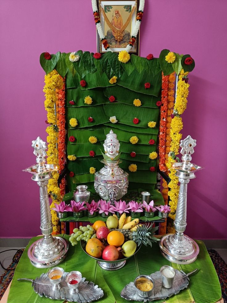 an arrangement of fruits and silver wares on a green table cloth in front of a purple wall