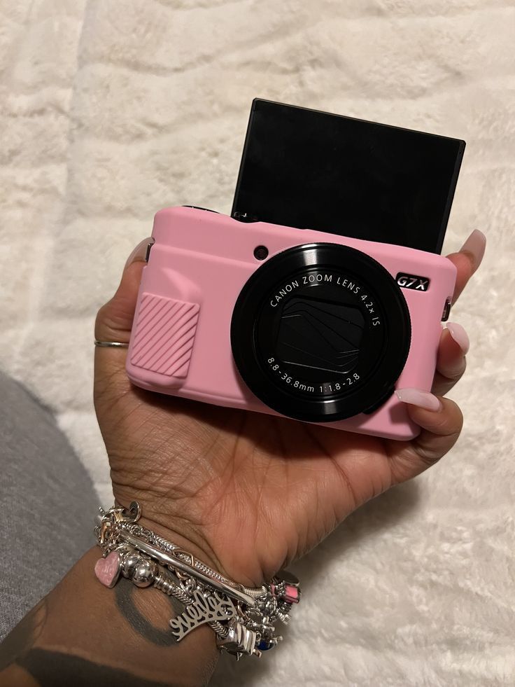 a person holding a pink camera in their hand with a chain around it's wrist