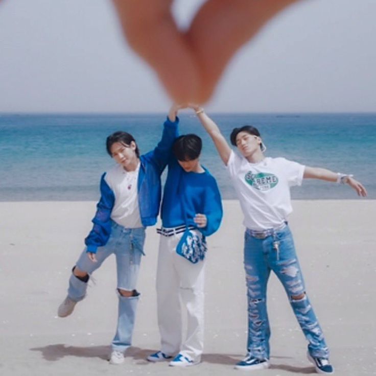 three young men standing on top of a sandy beach next to the ocean with their hands in the air