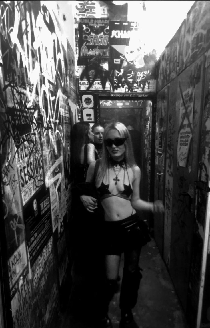 a woman in short skirt and boots walking down a narrow hallway with graffiti on the walls