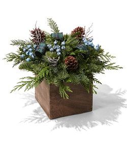 a wooden vase filled with blue flowers and greenery on top of a white surface