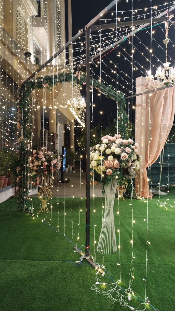 an outdoor wedding venue decorated with string lights and flowers in a vase on the grass