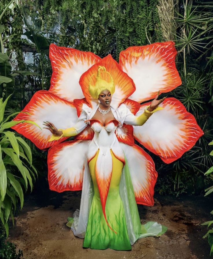 a woman is dressed as a flower in front of some trees and bushes with her arms outstretched