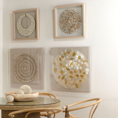 three framed art pieces hang on the wall above a glass table with two wicker chairs