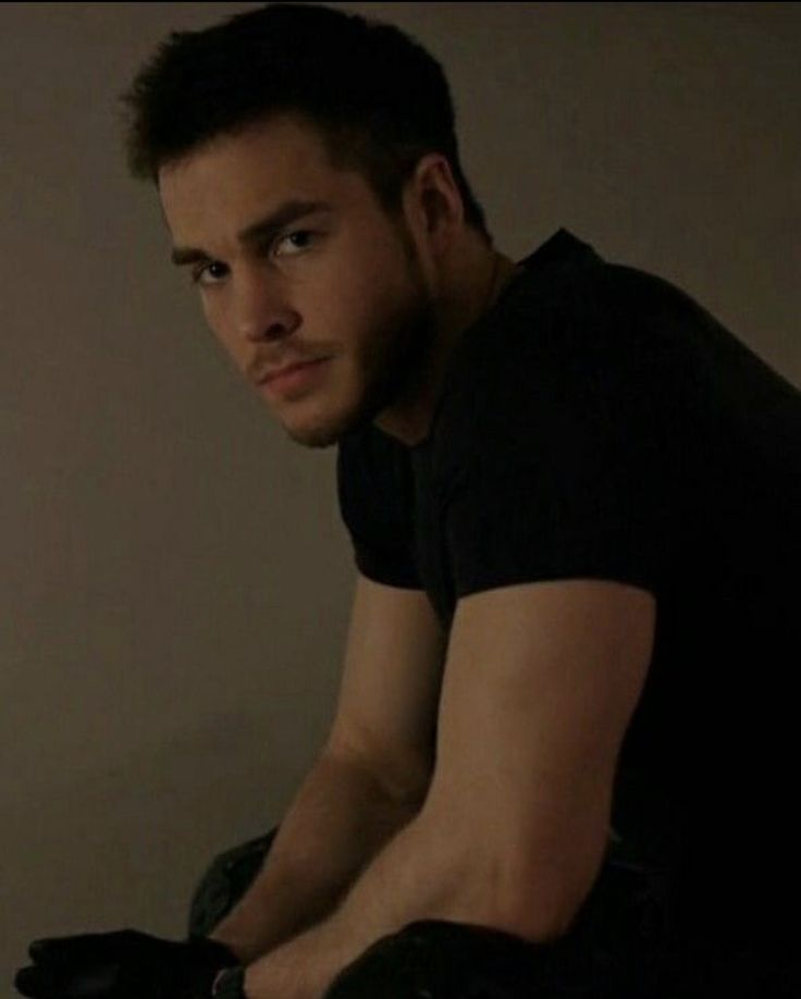 a man in black shirt sitting on top of a chair next to a wall and looking at the camera