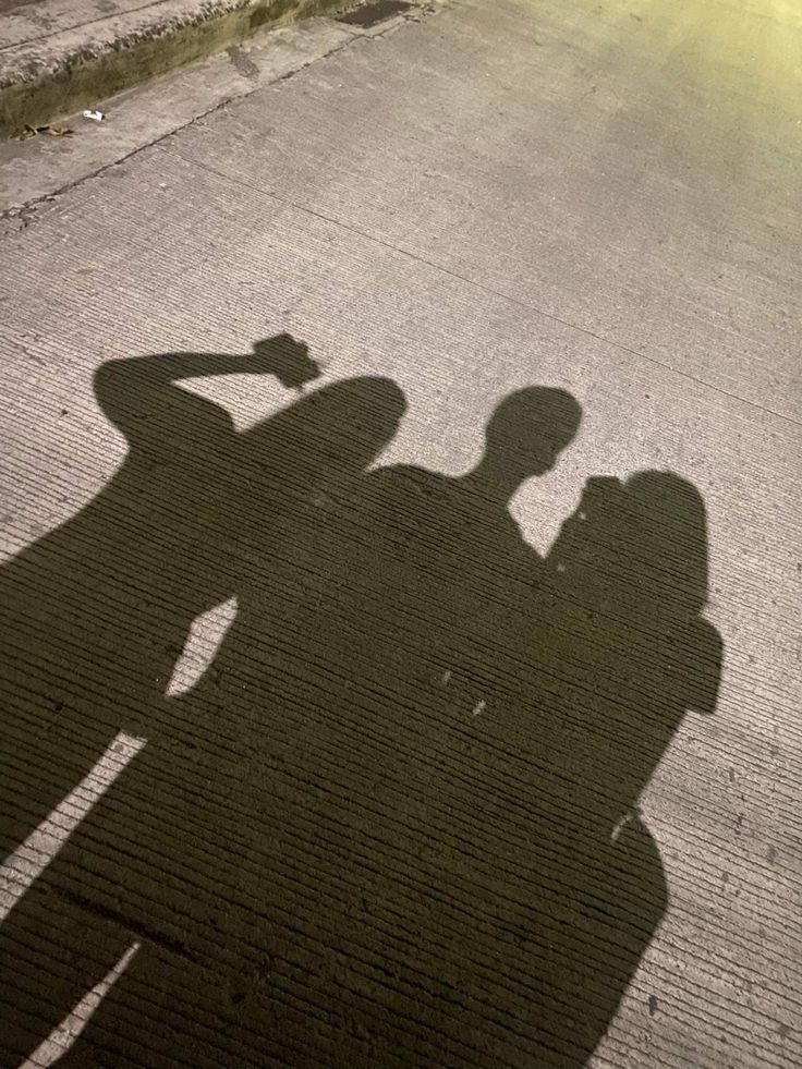 two people standing next to each other in the street with their shadows on the ground