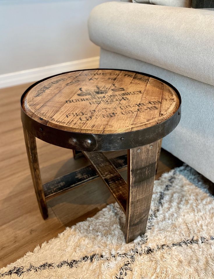 a round wooden table sitting on top of a white rug next to a gray couch