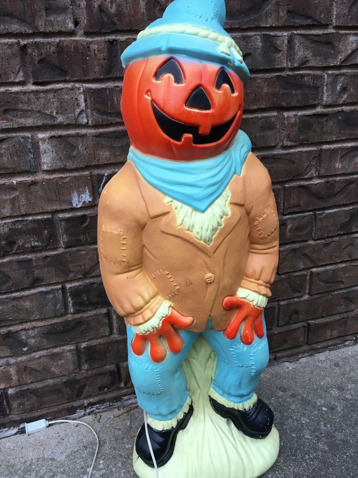 a statue of a scarecrow with an orange pumpkin on it's head and blue pants