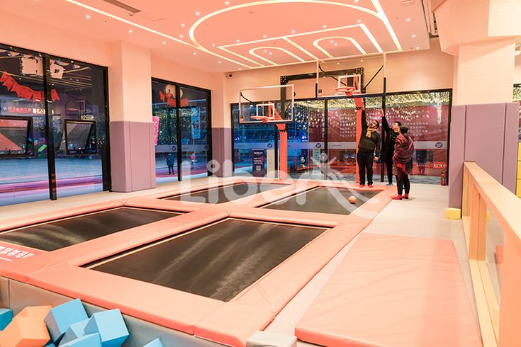 an indoor trampoline gym with two people walking in the doorway and one person on the other side