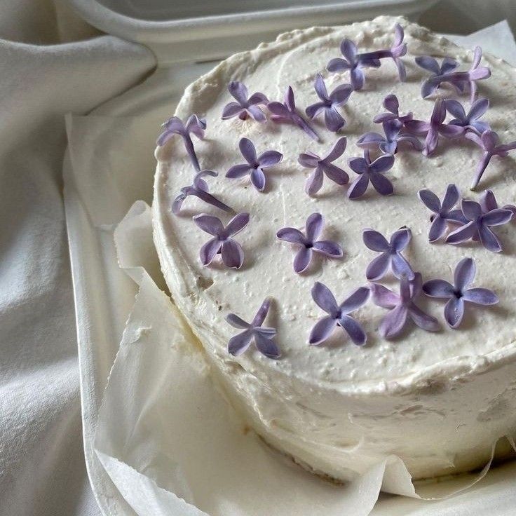 a cake with white frosting and purple flowers sitting on top of a paper towel