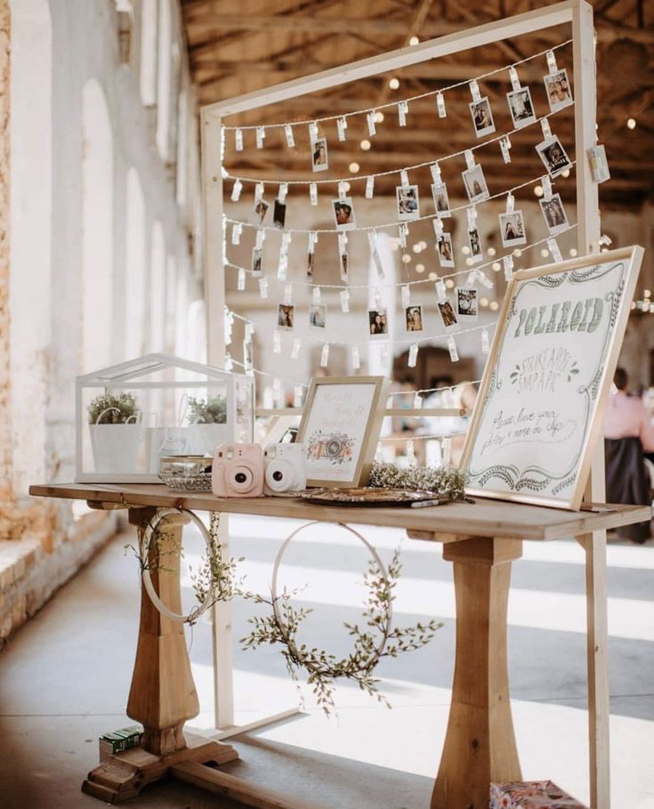 a wooden table topped with pictures and lights next to a white wall covered in string lights