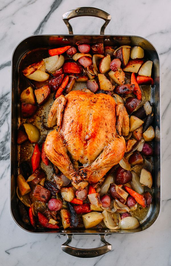 a roasting pan filled with chicken, potatoes and carrots on a marble counter top