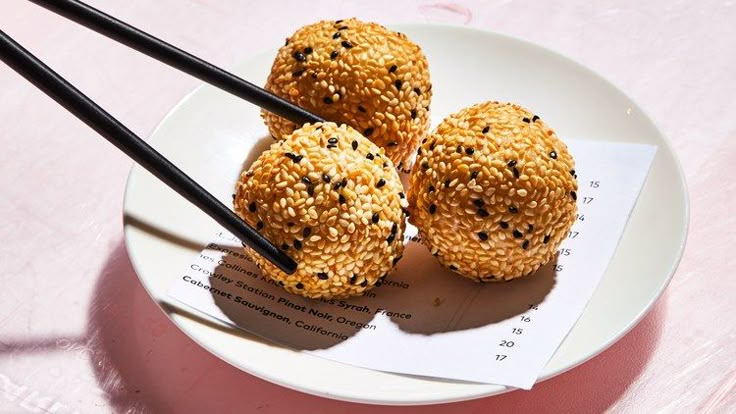 three sesame seed balls on a plate with chopsticks sticking out of the middle