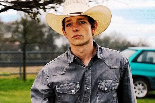 a man wearing a cowboy hat standing in front of a car