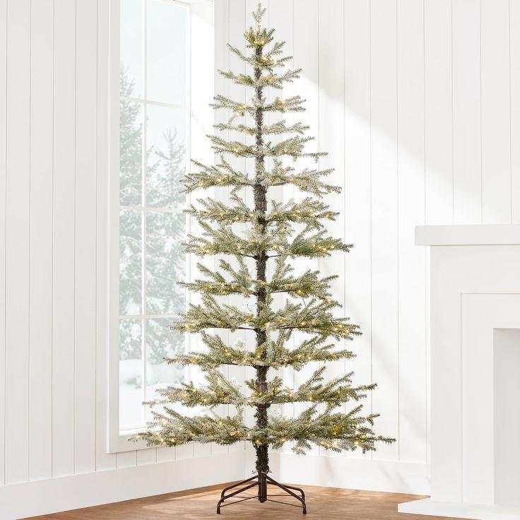 a small white christmas tree in front of a window with snow on the ground and wood flooring