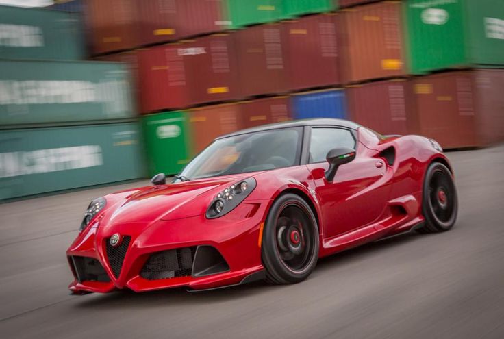 a red sports car driving down a street next to shipping containers on the side of the road