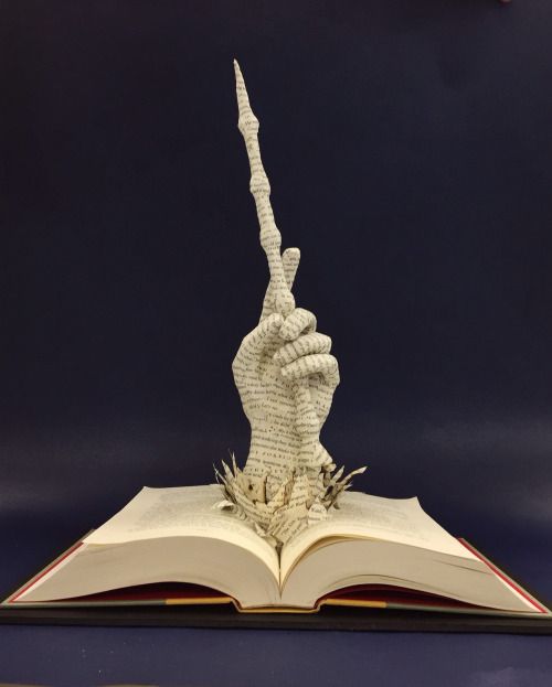 an open book with a sculpture of a hand holding a pen on top of it