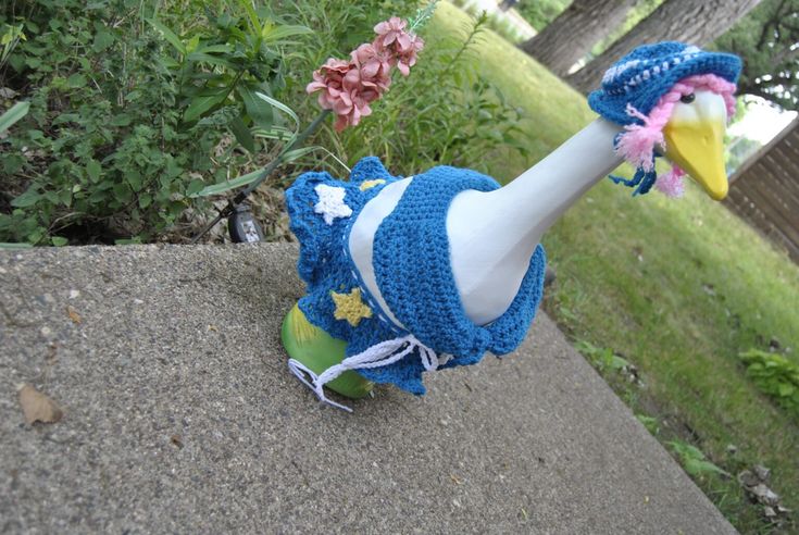 a stuffed bird wearing a blue hat on top of a cement wall next to flowers