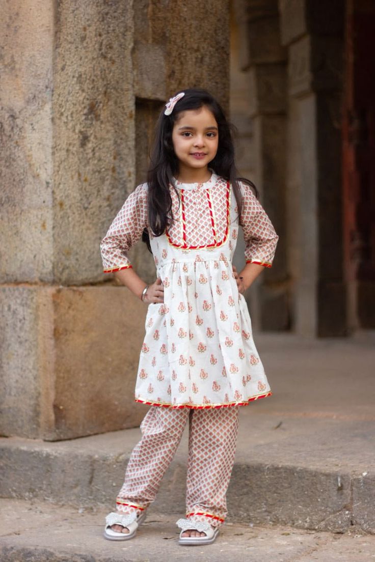 "Perfect for summer weddings and festivals this lehengha and top (set of 2) is an eye turner. Shouting with oodles of comfort during the festivities this cotton peplum suit is going to make your little one feel like herself while enjoying the festive season. Kurta - White base with pink floral print. Stand collar and embellished yoke. Payjama - Printed floral payjama makes it a comfy wear for your little ones as it comes with elasticated waist with drawstring for easy wear. Floral print  Fabric Festive Bollywood Cotton Dress, Fitted Cotton Salwar Kameez For Puja, Cotton Sets With Printed Motifs For Diwali, Fitted Cotton Palazzo Set For Diwali, Festive Cotton Block Print Sharara, Fitted Cotton Palazzo Set For Festive Occasions, Fitted Cotton Sets For Festive Occasions, Cotton Anarkali Salwar Kameez For Puja, Bollywood Style Cotton Sets With Block Print